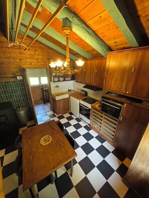 A kitchen with a checkered floor, wooden cabinets, a table, and a hanging light fixture. - Comfortable chalet for nature lovers - near Portes du Soleil skiing area (Val-d'Illiez)