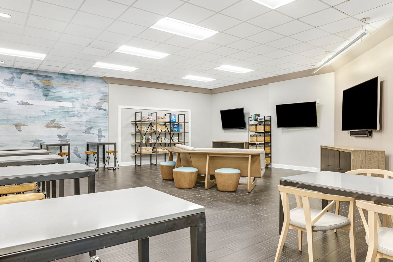 A classroom with tables, chairs, a bookshelf, and a mural on the wall.