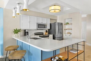 Une cuisine moderne avec des meubles blancs, des appareils en acier inoxydable et un îlot central doté de tabourets de bar.