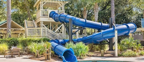 A pool area with a water slide structure and a small building with a balcony.