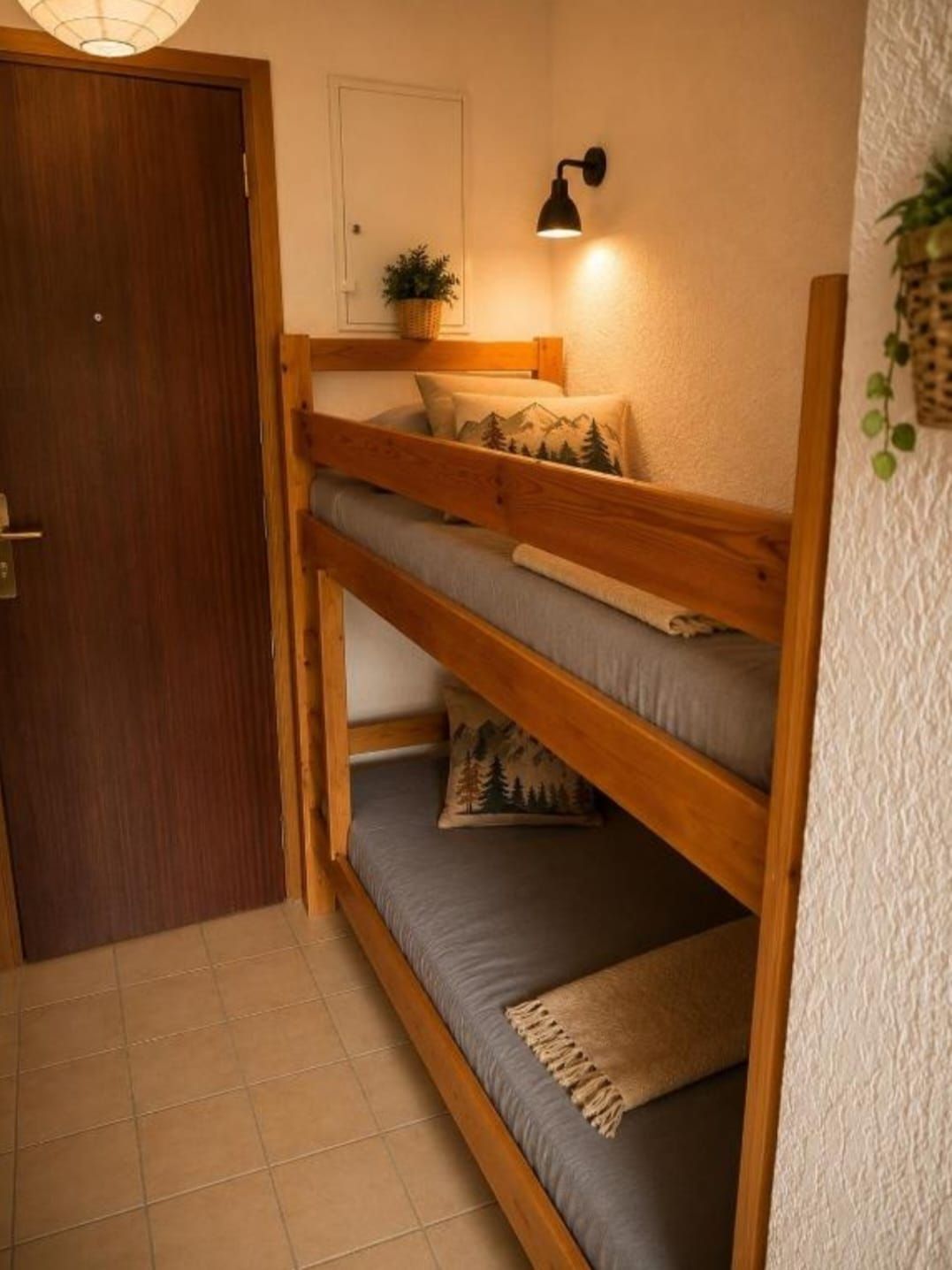 Uma cama de beliche com cabeceira, uma luminária fixada na parede e uma porta.