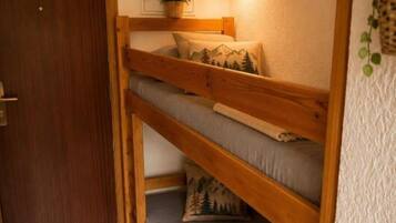 Uma cama de beliche com cabeceira, uma luminária fixada na parede e uma porta.