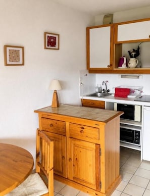 Een functionele keuken met houten kastjes, een spoelbak en een eethoek met een tafel en stoelen.