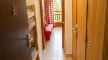 Um corredor com uma porta de madeira à esquerda, um sofá vermelho ao fundo e um guarda-roupa de madeira à direita.