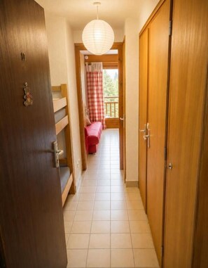 Een gang die uitkomt op een balkon, met een geruit gordijn, houten deuren en een hangende lamp.