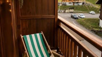 Un balcon doté d’une balustrade en bois, d’un fauteuil de jardin à rayures vertes et blanches, et d’une vue sur une route et des bâtiments au loin.