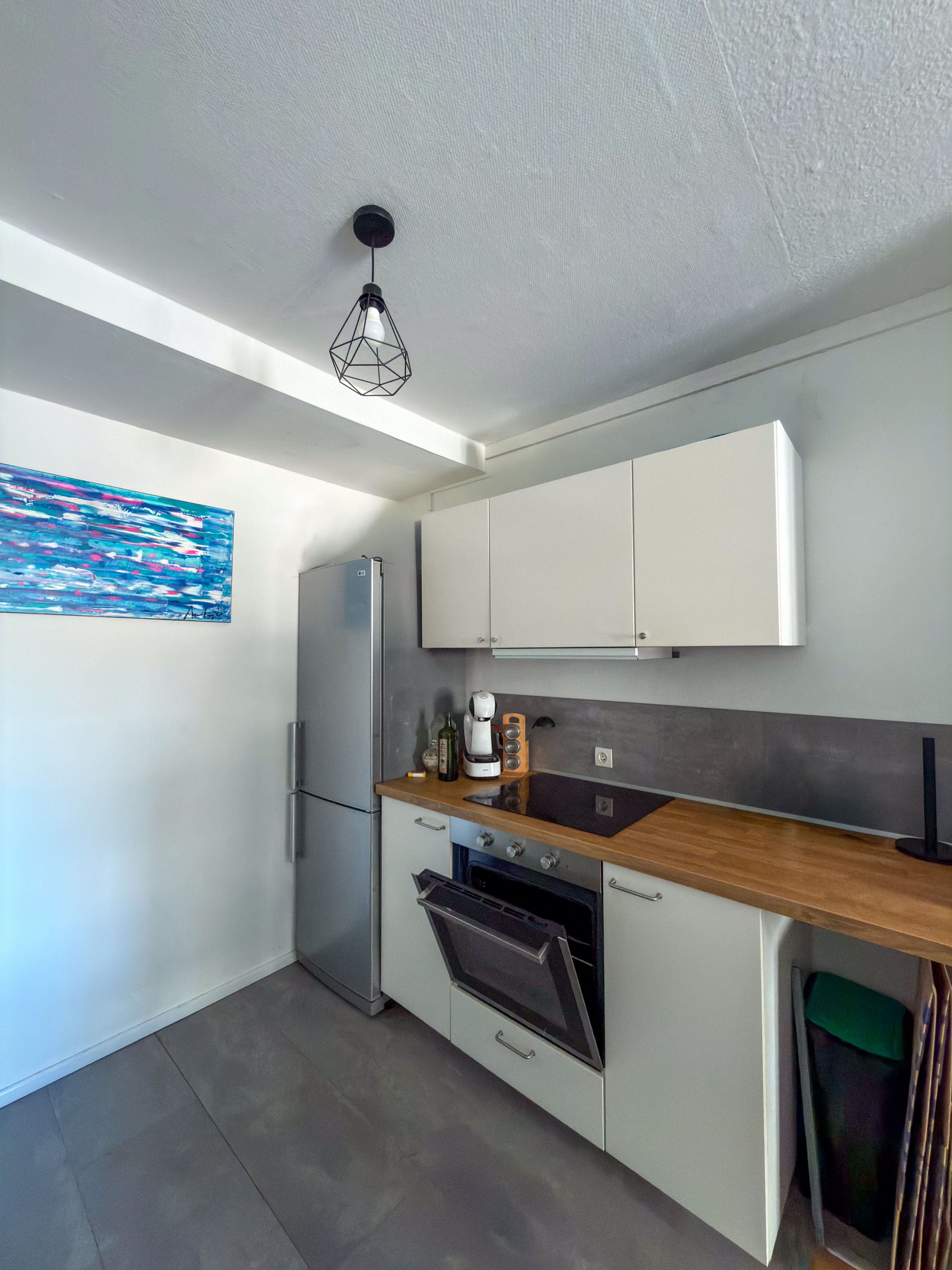 A modern kitchen with white cabinets, a built-in oven, and a wooden countertop.