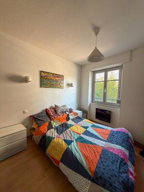 A bedroom with a bed, a window, a wall-mounted artwork, and a ceiling light. - Spacious one-bedroom apartment near downtown (Strasbourg)