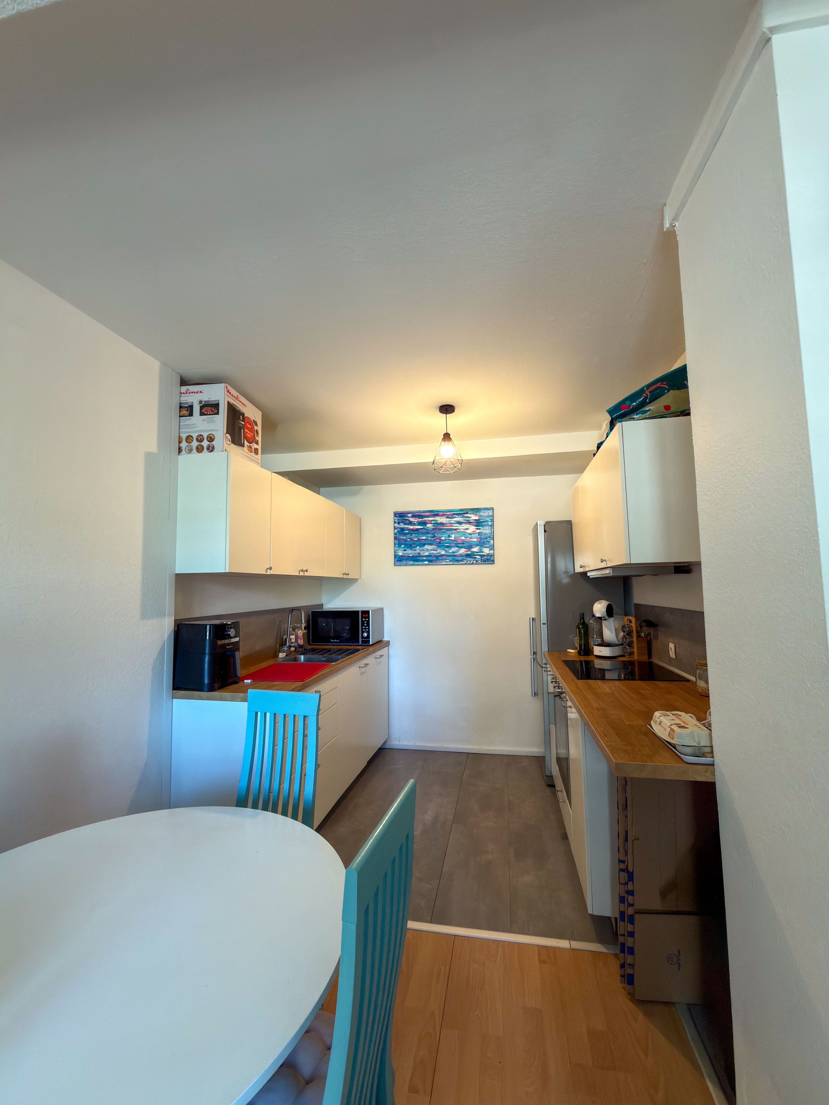 A compact kitchen with white cabinets, a microwave, a coffee maker, and a dining table with chairs.