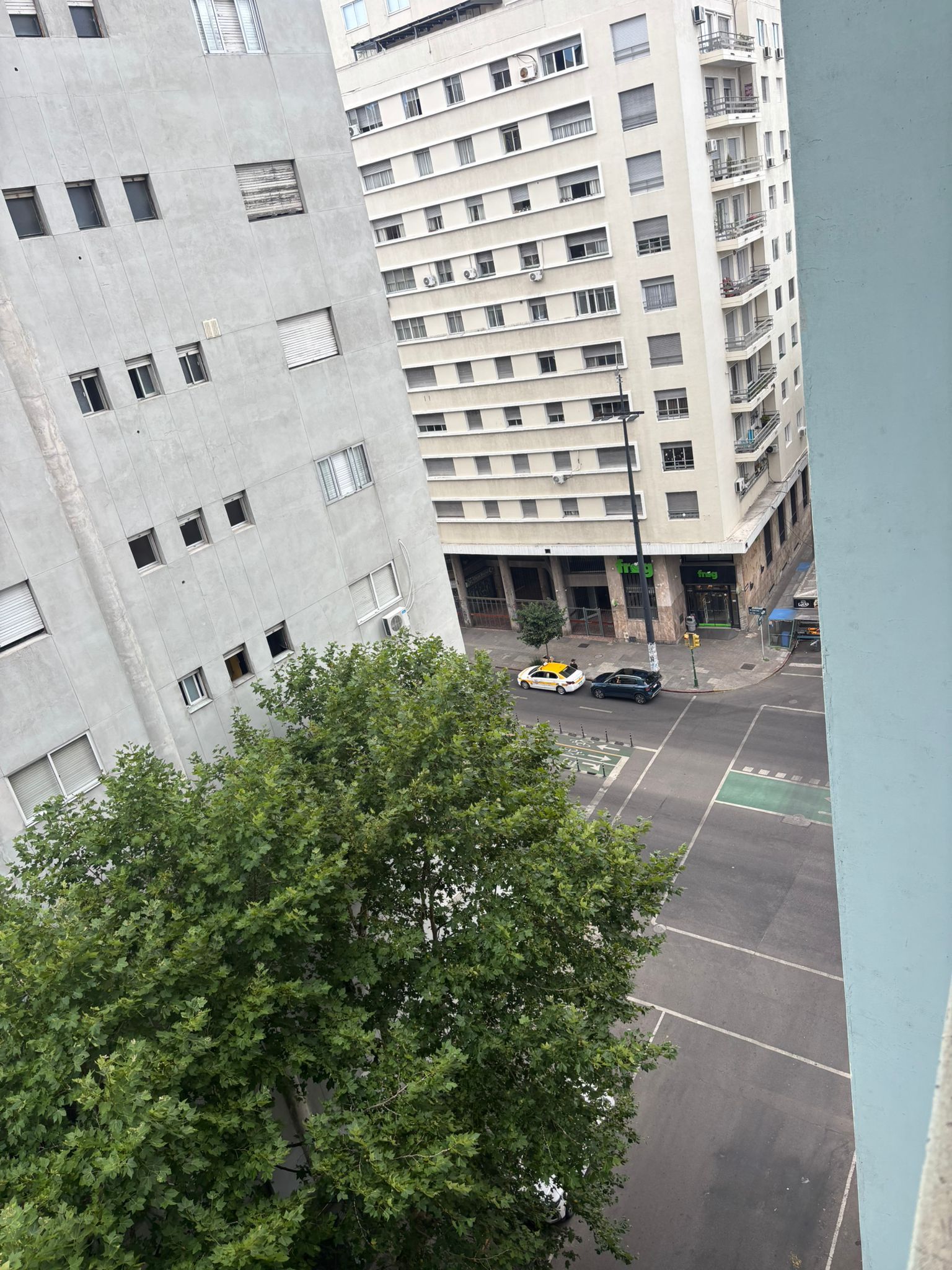 Un edificio de varios pisos con estacionamiento y un árbol al frente.