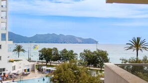 A pool area with a view of the sea and mountains, surrounded by trees and a building. - Cozy Beachfront 1-Bedroom Apartment in Cala Millor, Mallorca with Sea Views & AC (Cala Millor)