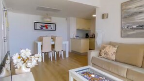 A living room with a sofa, a coffee table with decorative items, a dining area with chairs, and a kitchen in the background. - Cozy Beachfront 1-Bedroom Apartment in Cala Millor, Mallorca with Sea Views & AC (Cala Millor)
