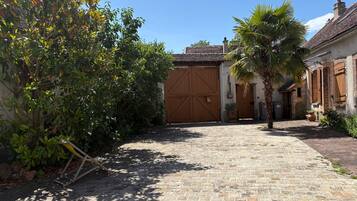 Un patio empedrado con un gran portón de madera, rodeado de vegetación y edificios.