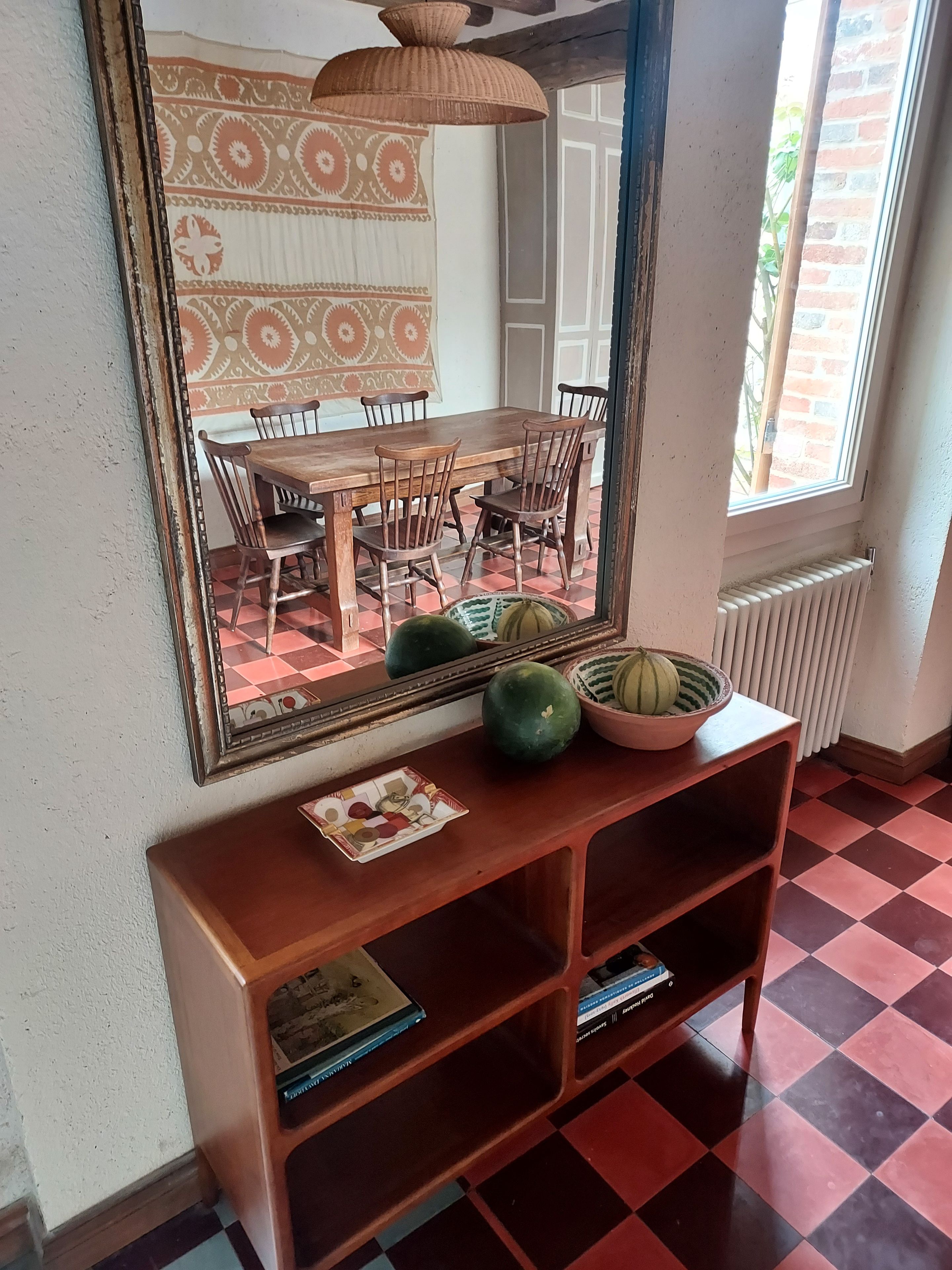 Un comedor con una mesa y sillas de madera, un espejo en la pared y un suelo a cuadros.