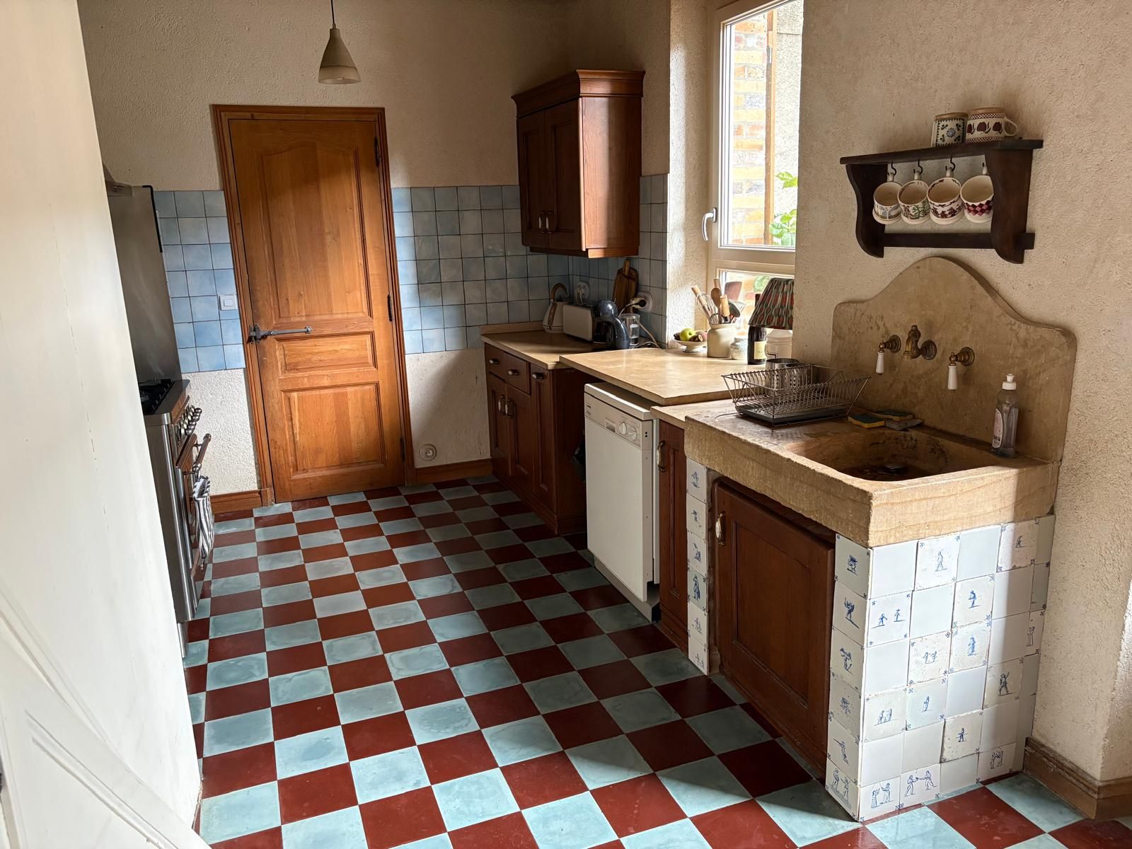 Uma cozinha com piso xadrez, armários de madeira, uma pia e uma janela.