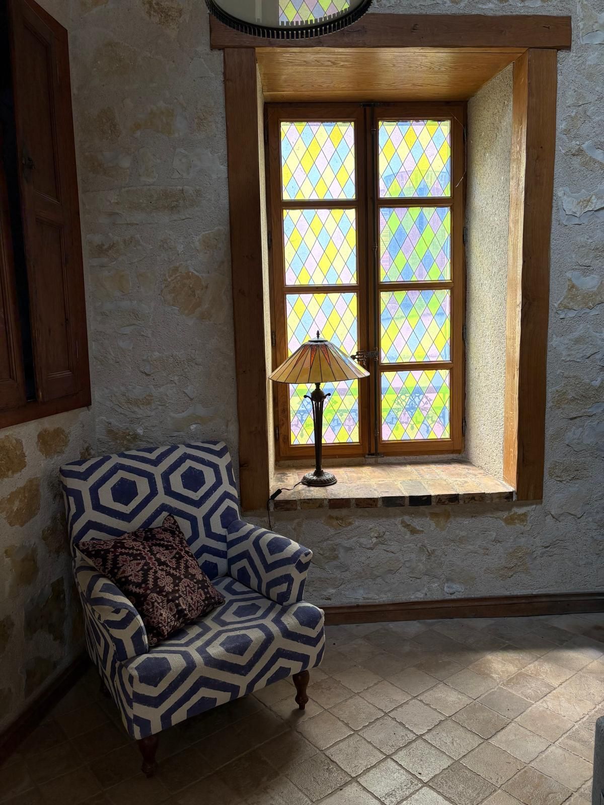 Een kamer met een gestreept fauteuil, een raam met glas-in-lood en een lamp op de vensterbank.