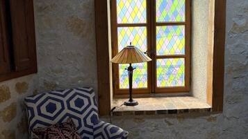 Una habitación con un sillón estampado, una ventana con vidrieras y una lámpara en el alféizar.