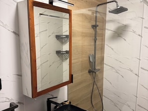A bathroom with a wooden-framed mirror, a shower with a handheld showerhead, and marble-patterned walls. - Monte Cara (Mindelo)
