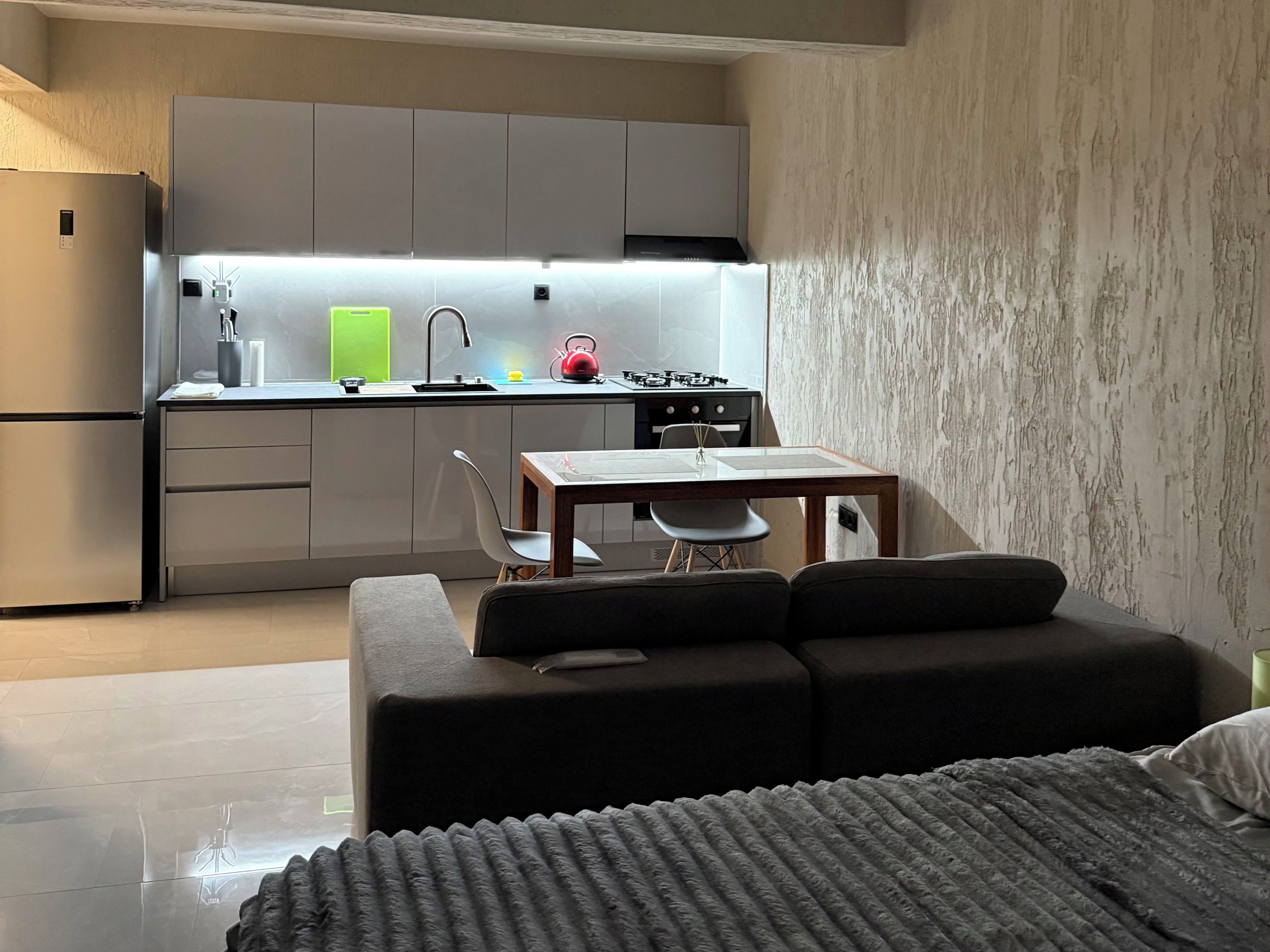 A modern kitchen with grey cabinets, a dining table with chairs, and a sofa in the foreground.