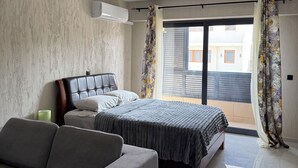 A bedroom with a bed, a sofa, a window with curtains, and an air conditioning unit. - Monte Cara (Mindelo)