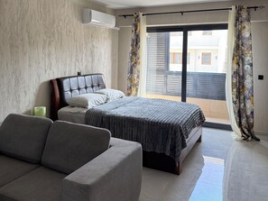 A bedroom with a bed, a sofa, a window with curtains, and an air conditioning unit. - Monte Cara (Mindelo)
