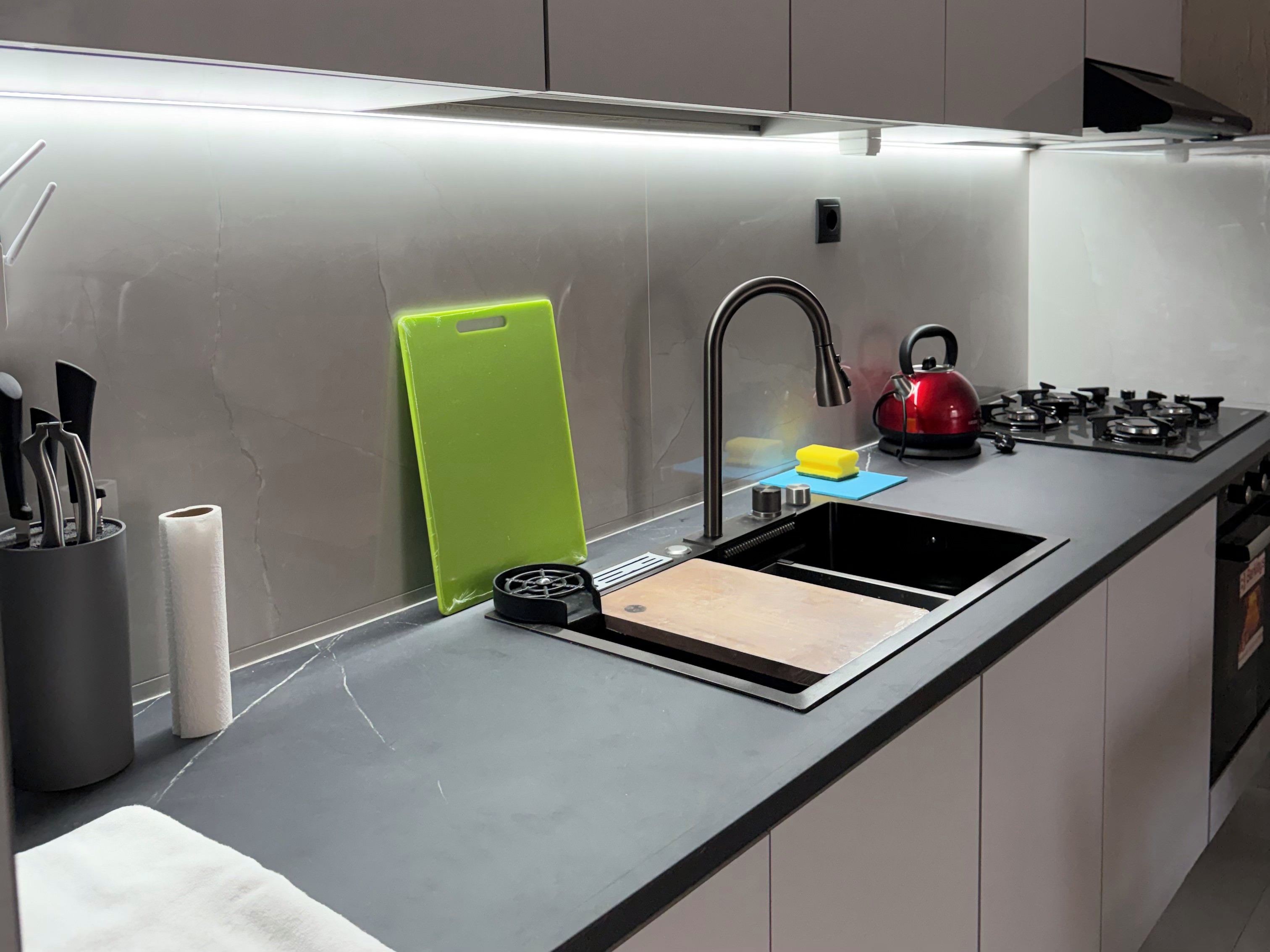 A modern kitchen with a stainless steel sink, a kettle, and a gas stove.