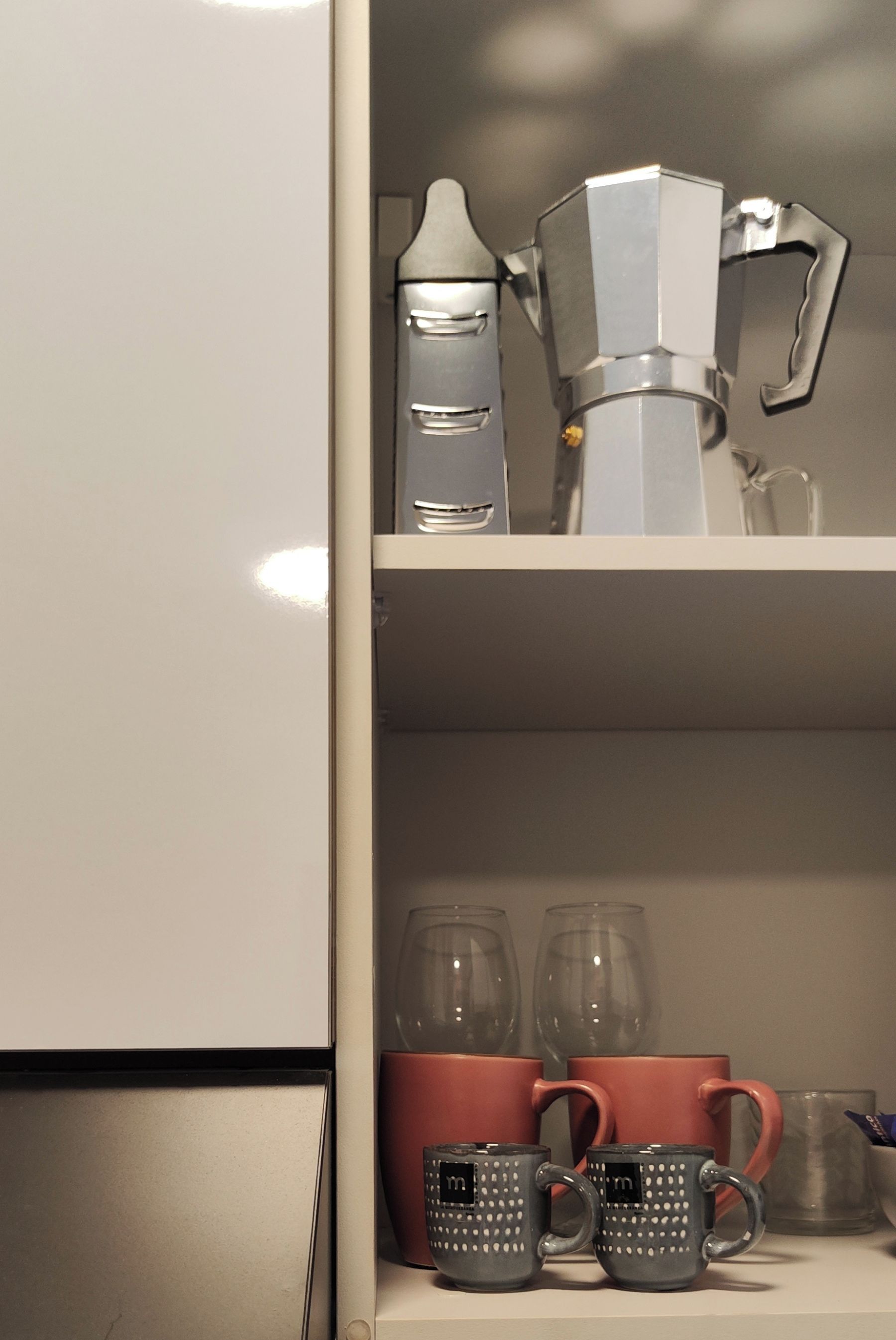A kitchen with a coffee maker, a kettle, and two shelves with mugs and glasses.
