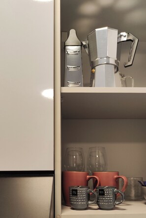 A kitchen with a coffee maker, a kettle, and two shelves with mugs and glasses.