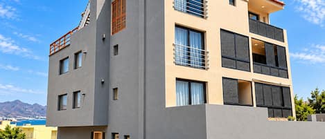 A modern multi-story building with balconies, large windows, and a flat roof.