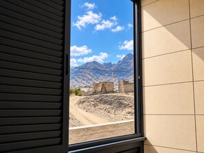 A window with a view of a mountainous landscape, a dirt path, and some buildings.