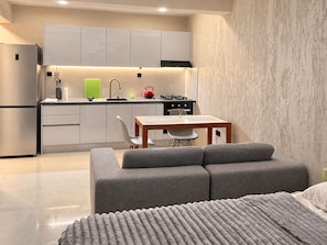 A compact kitchen with modern appliances, a dining area with a table and chairs, and a grey sofa in a living space.