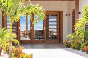 A covered outdoor seating area with a view of the ocean, wooden doors, and tropical plants. - Luxury Oceanfront 5-Bedroom Villa with Private Pool | Bonaire (Kralendijk)