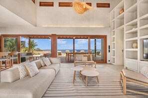 A spacious living area with a large sofa, coffee table, and a view of the ocean through large sliding doors. - Luxury Oceanfront 5-Bedroom Villa with Private Pool | Bonaire (Kralendijk)