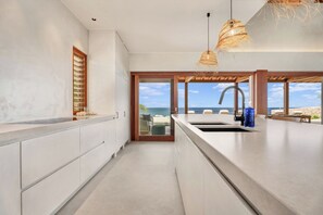 A modern kitchen with a large island, a view of the ocean, and a dining area with outdoor seating. - Luxury Oceanfront 5-Bedroom Villa with Private Pool | Bonaire (Kralendijk)