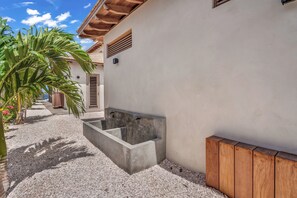 A concrete water feature adjacent to a building with a wooden deck and a gravel pathway. - Luxury Oceanfront 5-Bedroom Villa with Private Pool | Bonaire (Kralendijk)