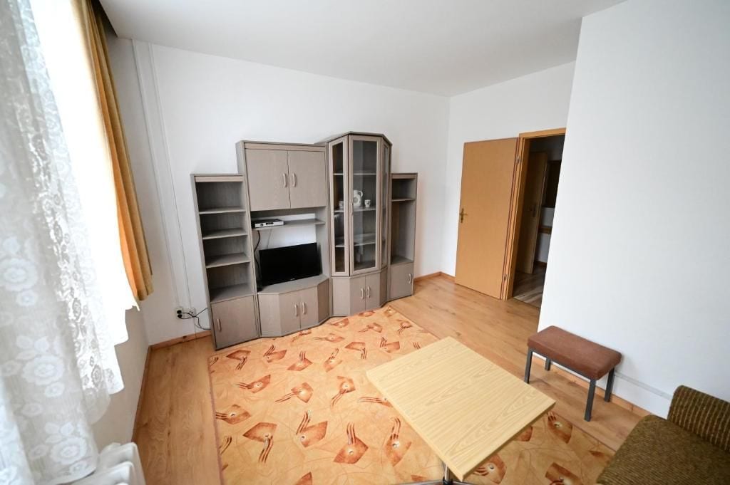 Een kamer met een houten vloer, een kast met glazen deuren, een bank en een deur naar een andere kamer.