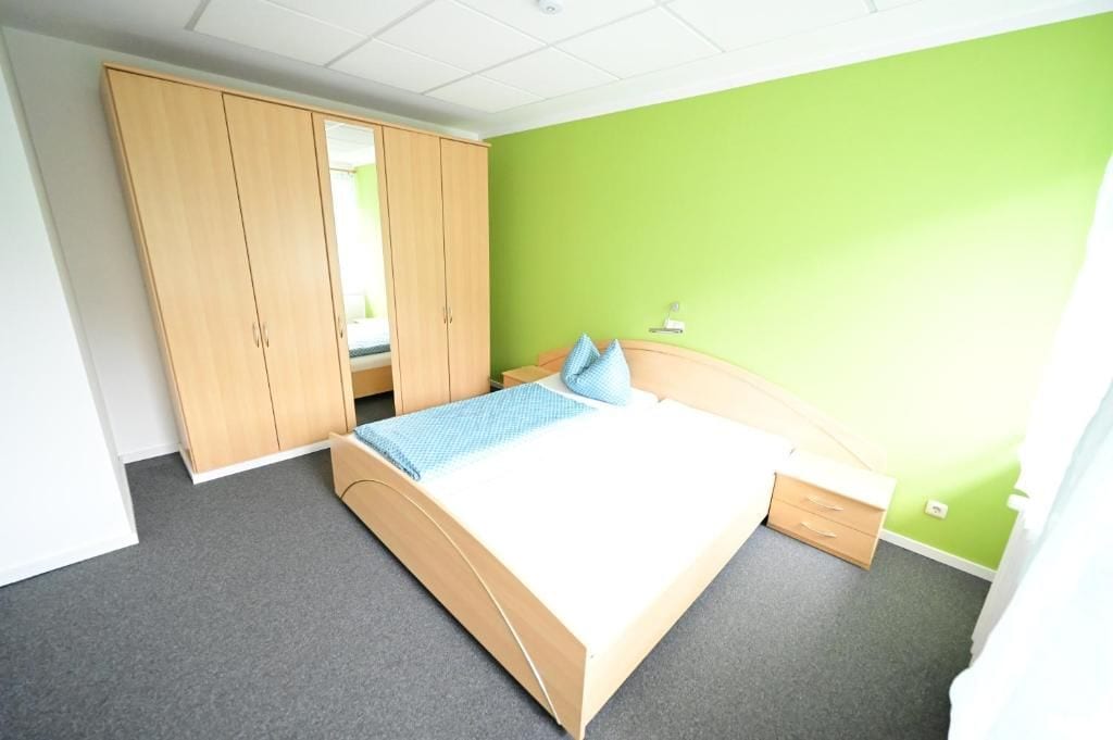 A bedroom with a bed, a wardrobe, a nightstand, and a green wall.