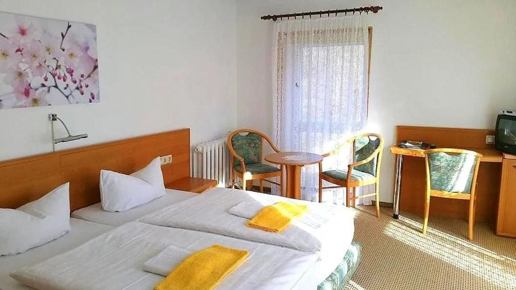 Habitación de hotel con dos camas, un escritorio, una silla, un televisor y una ventana con cortinas.