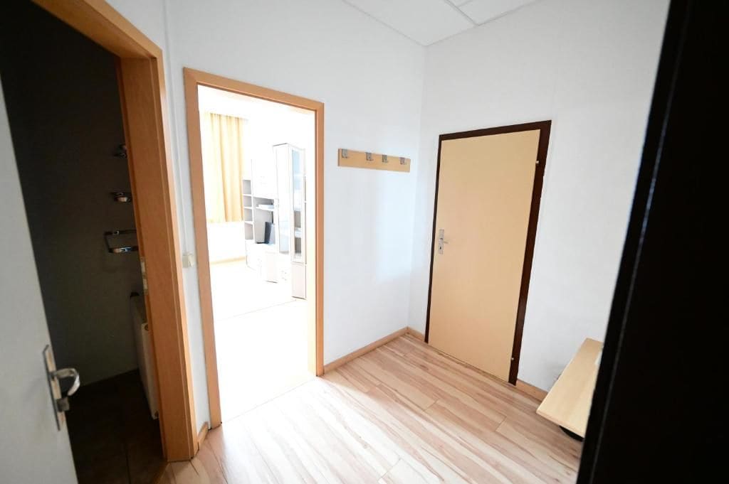 Una habitación con piso de madera, una puerta y un ventanal con cortinas.
