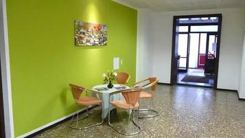 Una habitación con pared verde, un cuadro, una mesa con sillas y una puerta que da a otra zona.