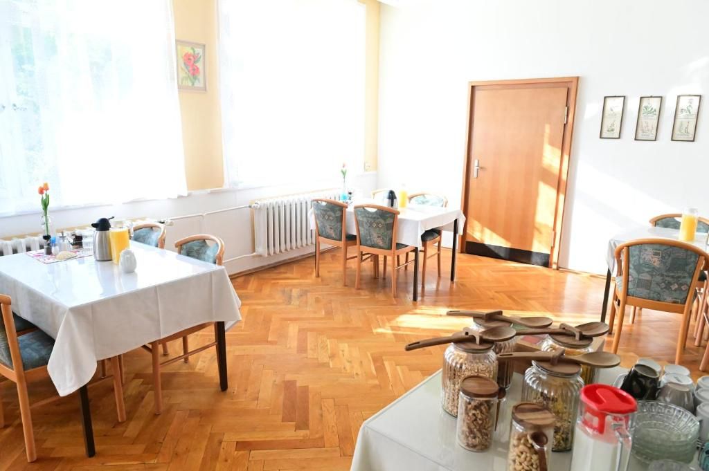 A dining area with wooden flooring, white tablecloths, and chairs. There are jars with lids on a table.