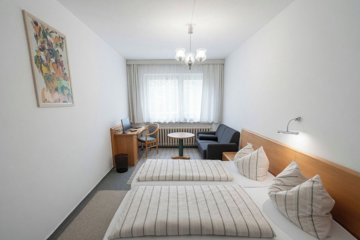 A hotel room with a bed, a desk, a chair, a sofa, and a window with curtains.