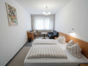 Una habitación de hotel con cama, escritorio, silla, sofá y ventana con cortinas.