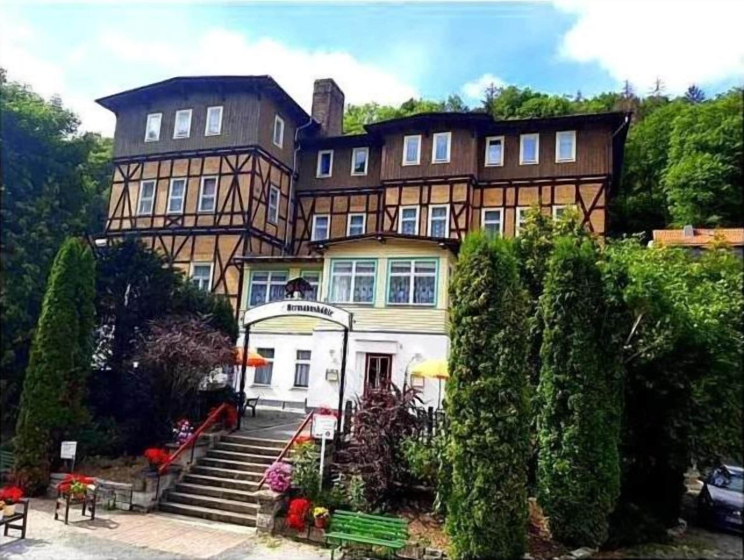 Un edificio con una escalera que conduce a una puerta, rodeado de vegetación y un banco.