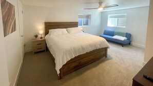 Quarto com cama de madeira, mesas de cabeceira, ventilador de teto e sofá azul.