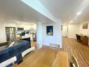 A modern kitchen with stainless steel appliances, a dining area with a wooden table and chairs, and a living room with a sofa and a coffee table.