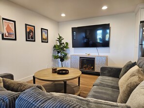 A living room with a fireplace, a television mounted on the wall, and framed pictures on the wall. - Powder Days & Cozy Nights: Family & Pet-Friendly 2BR 25 Min to Alta/Snowbird (Sandy)