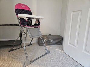 A high chair with a pink and black patterned seat, a white tray, and a Graco brand cover on the floor.