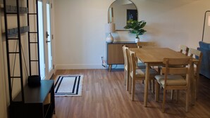 Uma sala de jantar com mesa e cadeiras de madeira, um tapete pequeno, uma planta e um espelho na parede.