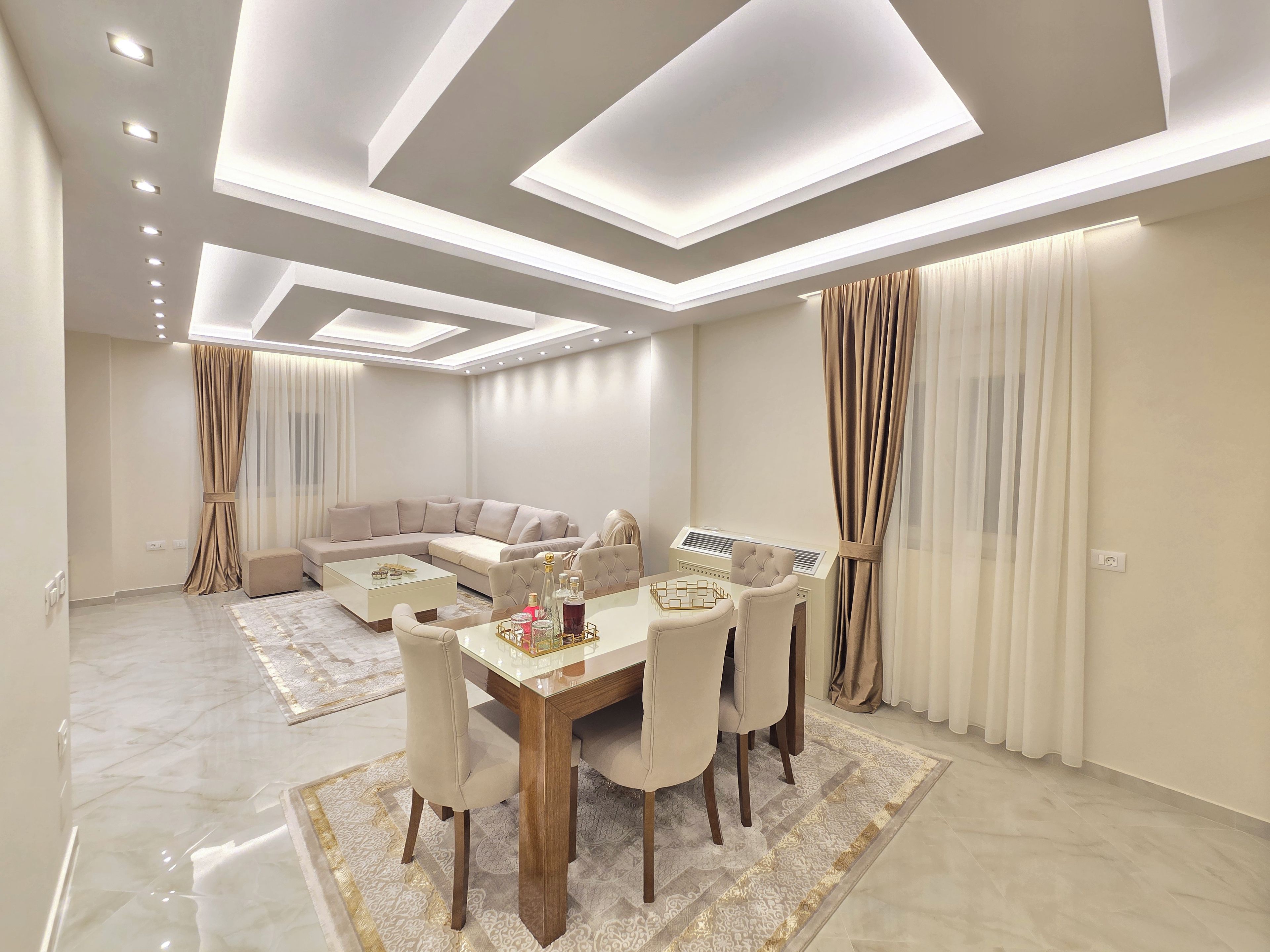 A modern living room with a sectional sofa, a dining table with chairs, and a ceiling with recessed lighting.